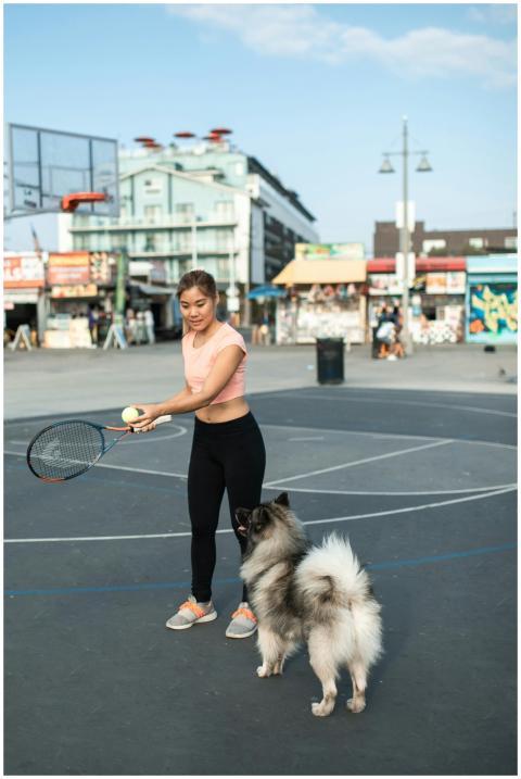 A woman playing tennis with her dog on an urban ou