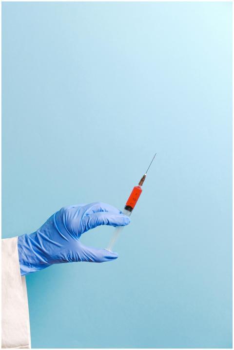 Gloved hand holding a syringe on a light blue back