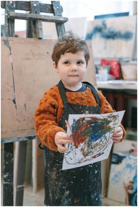 A young child displaying colorful artwork in an ar