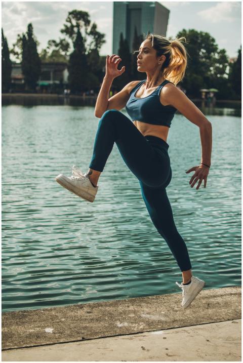 Active woman performing a fitness jump near a lake