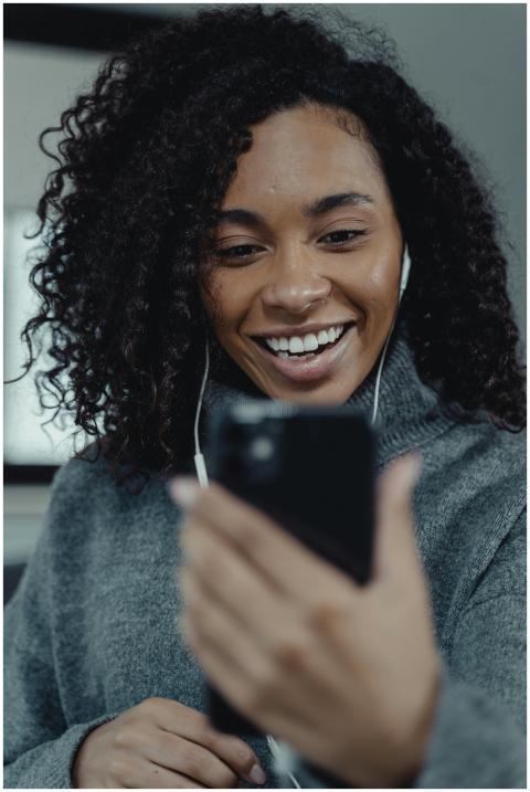 A joyful woman in a gray sweater uses a smartphone