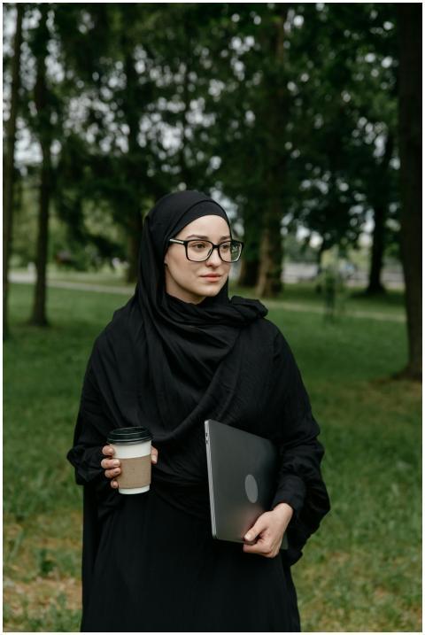 A young woman wearing a hijab and glasses holds a