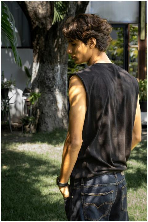 Young man in a sleeveless shirt stands outdoors un