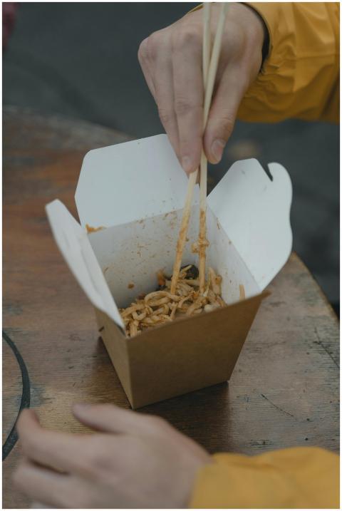 An individual enjoys Asian noodles from a takeaway