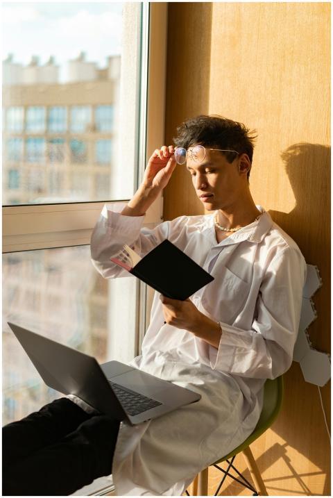 A young man in white attire reads by a bright wind