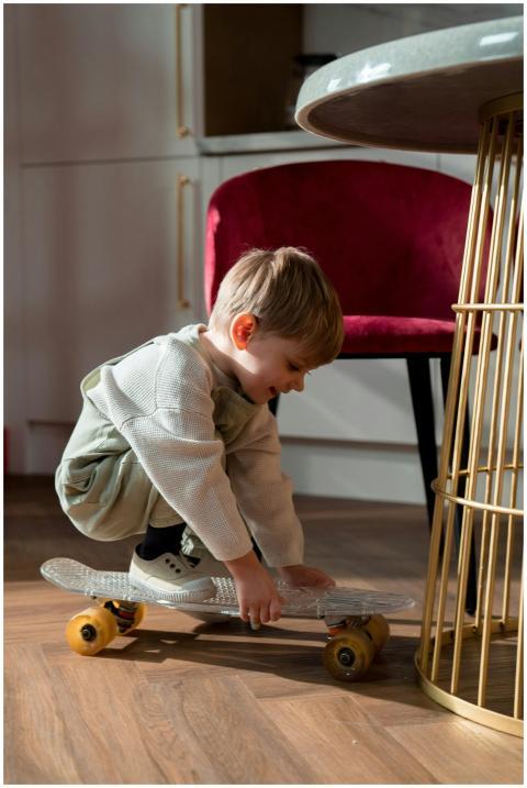A joyful child crouches on a skateboard in a livin