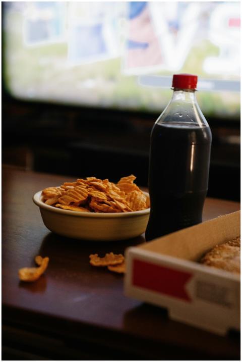 Bottle of cola between bowl with crunchy potato ch