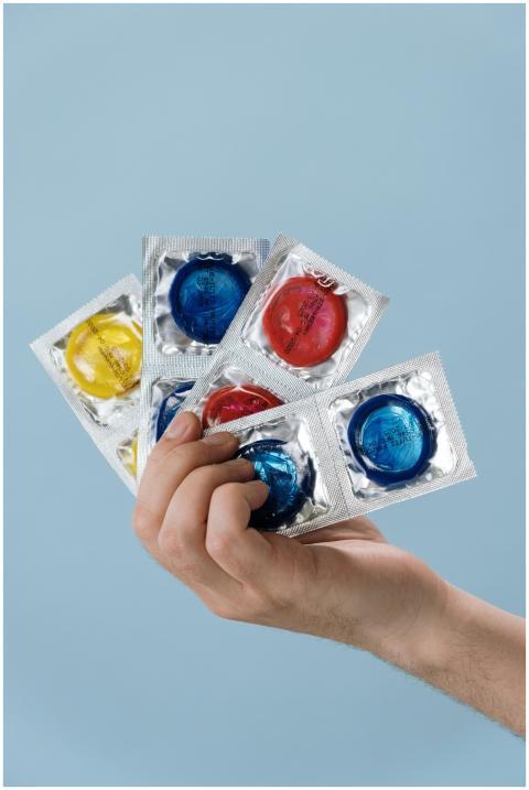 A hand holds multicolored condoms in foil packagin