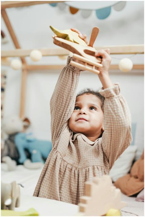 Happy child playing with wooden airplane indoors,