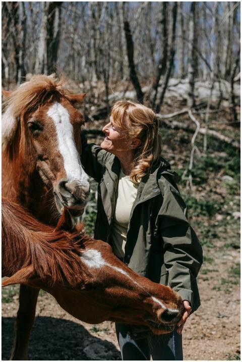 Smiling woman interacting with two horses in a lea