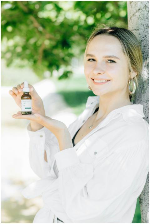 A young woman smiles while holding a CBD oil bottl