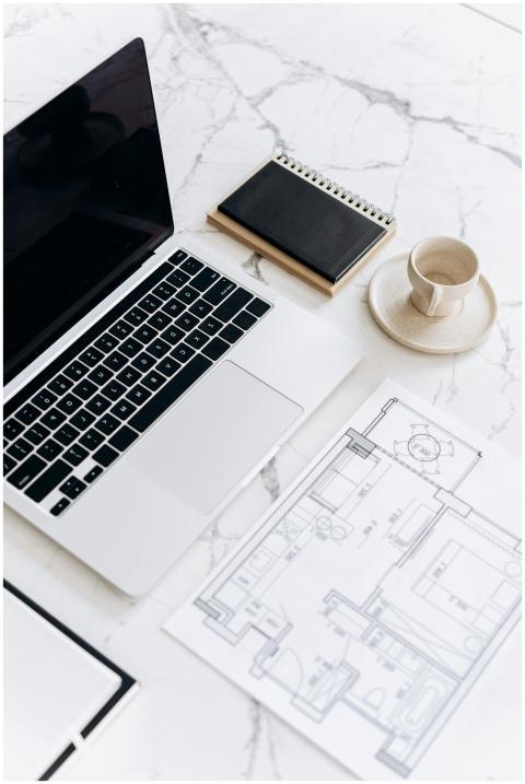 A clean, modern workspace with a laptop, blueprint