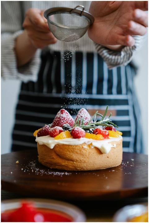 Closeup of a chef sprinkling powdered sugar on a c