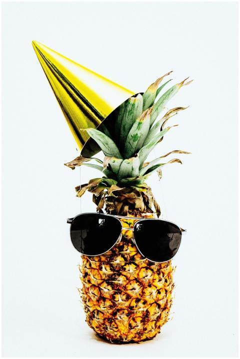 A pineapple dressed in sunglasses and a party hat,