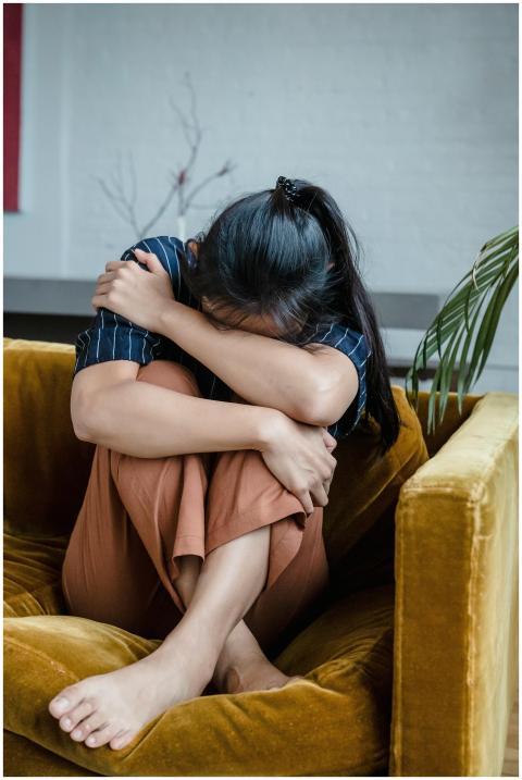 Adult woman hugging knees on mustard couch, repres