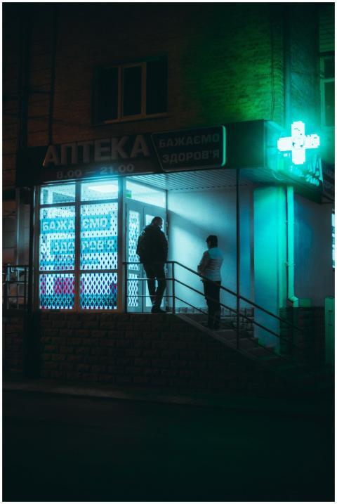 Two people standing outside an illuminated pharmac