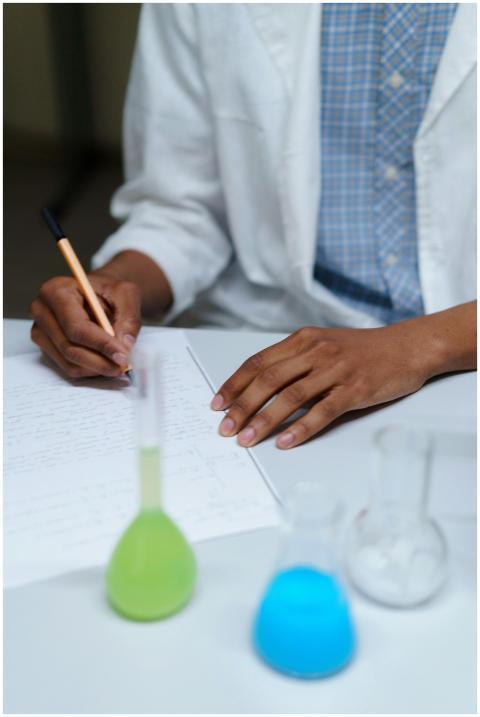 A student in a lab coat writes notes beside flasks