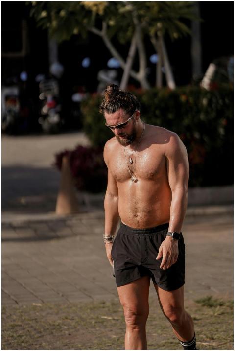 A shirtless man walking outdoors, showcasing a hea