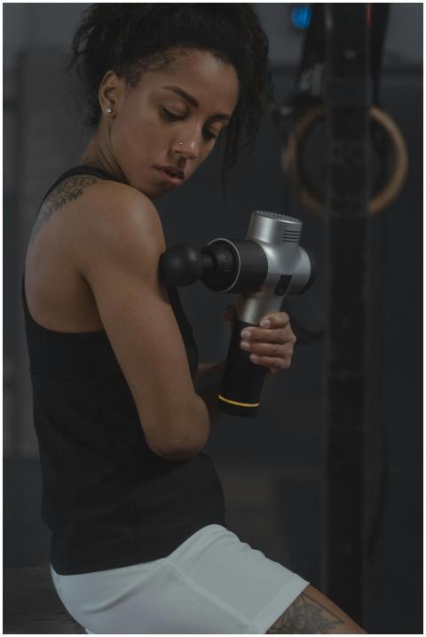 A woman in a gym uses a percussion massager on her