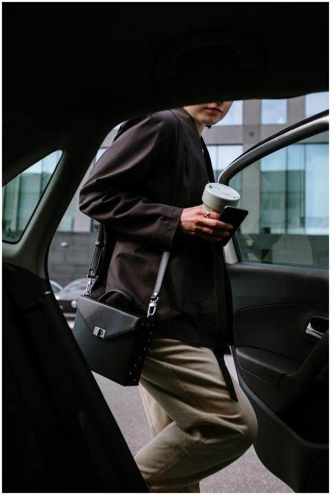 Stylish woman entering a car, holding coffee and s