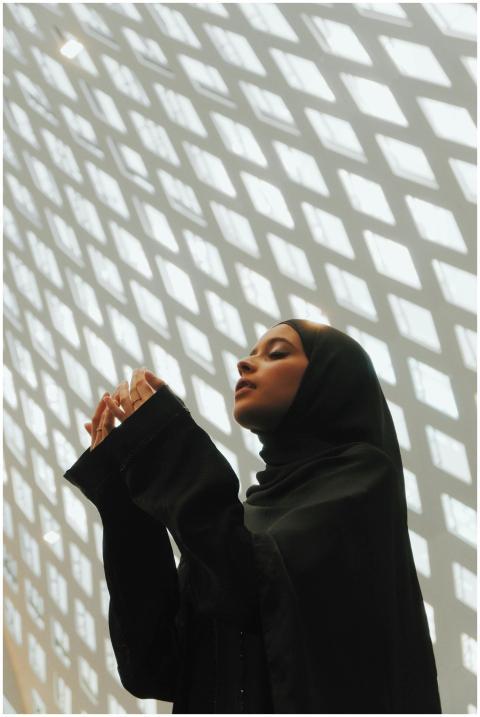 A Muslim woman in a hijab prays under an artistic