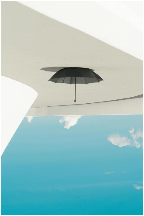 A black umbrella hanging upside down against a cle