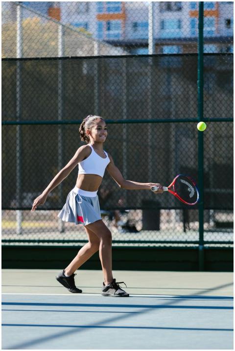 A young girl in activewear playing tennis on an ou