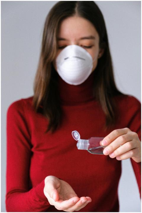 A woman indoors uses hand sanitizer while wearing