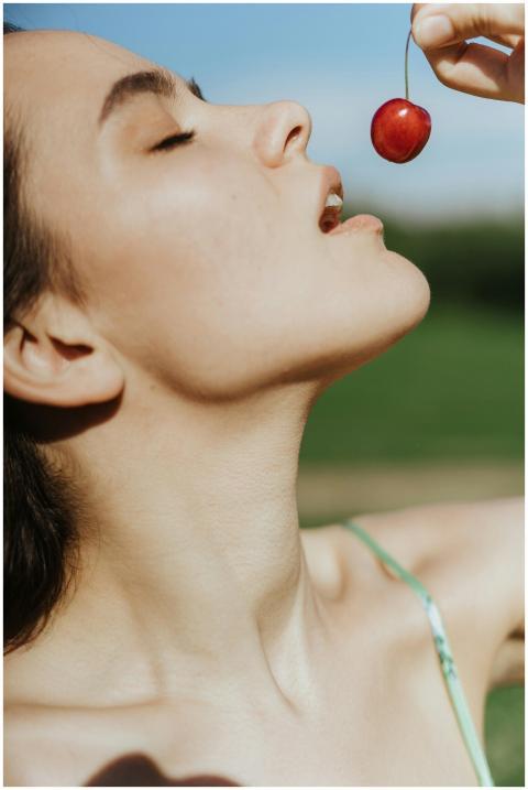 A woman poses under a clear sky, savoring a ripe c