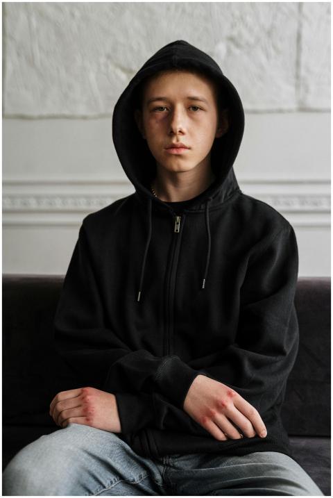 Teenager in black hoodie sitting indoors, contempl