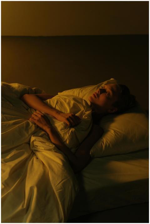 A serene woman rests in bed amidst warm, subdued l