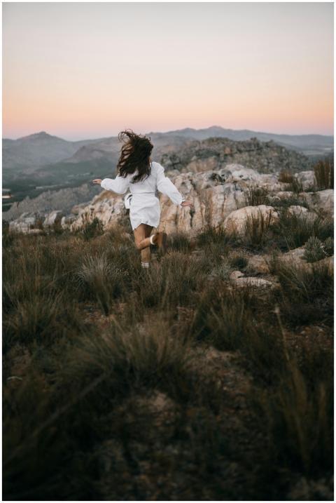 A woman runs through a rocky field with mountains