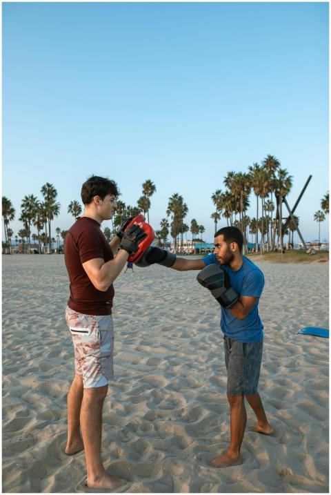 Two men engaged in a boxing workout on a sandy bea