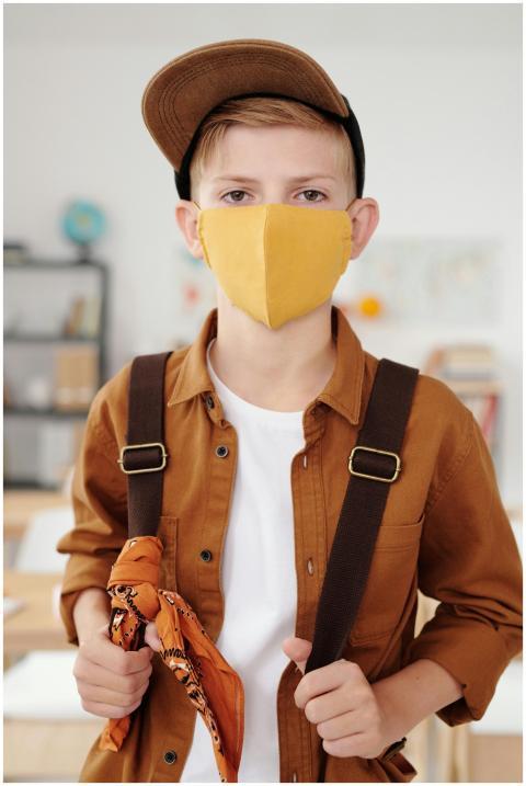 A young boy with a backpack and face mask in a cla
