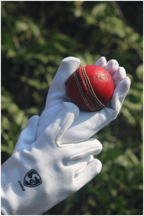 Close-up of a red cricket ball held in white glove