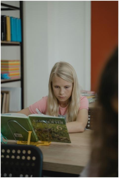 Blonde girl intently reads a book at school desk,