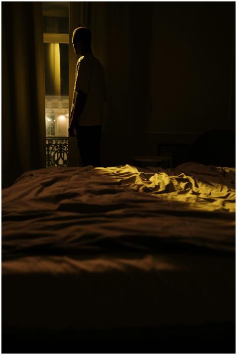 Person standing in a dimly lit bedroom, gazing out