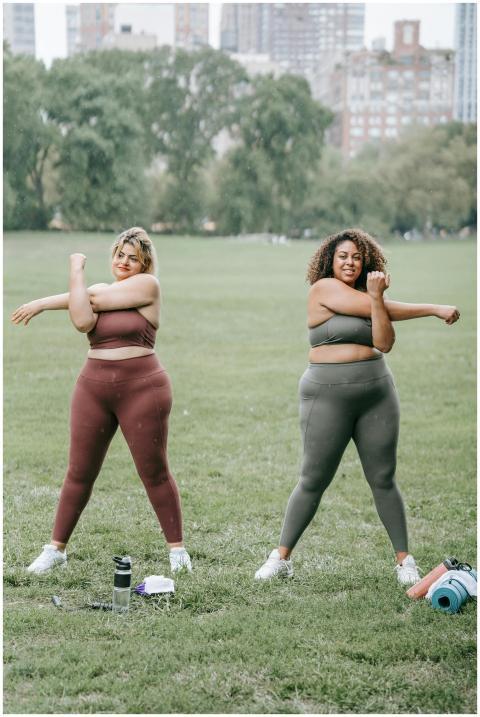 Two women in sportswear stretching in a grassy cit