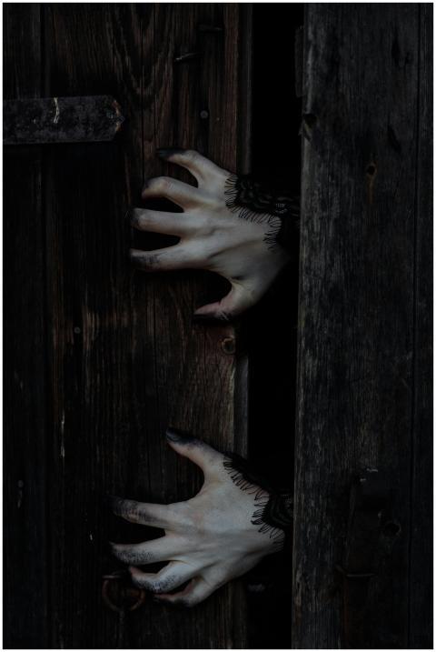 Eerie white hands with black nails reach through a