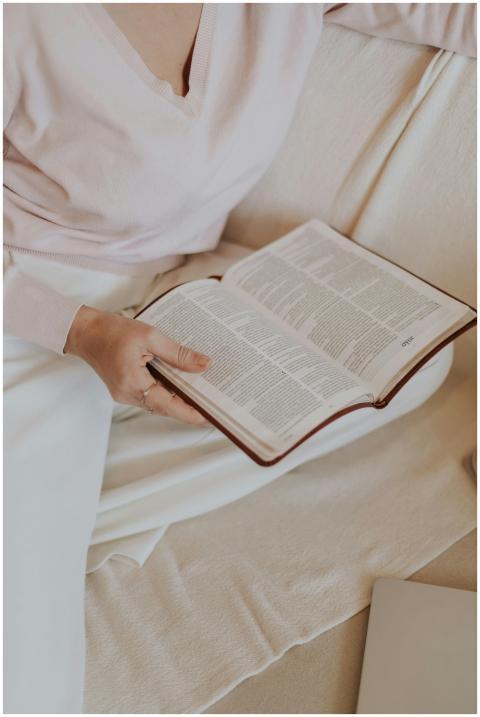 A woman in a pink sweater reading a book on a beig