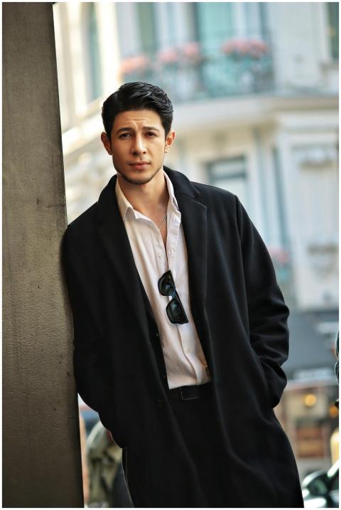 Stylish man in coat leaning against a building wit