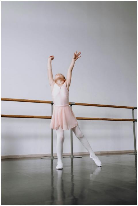 A young girl in a pink tutu gracefully stretches i