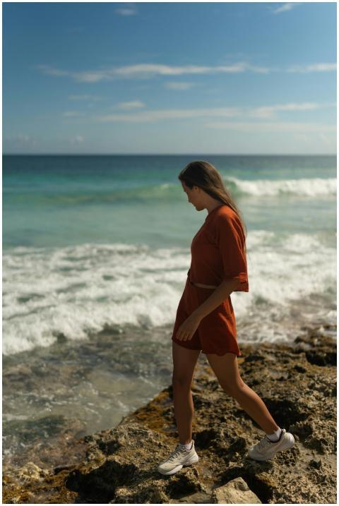 A woman in a red dress walks along a rocky beach u
