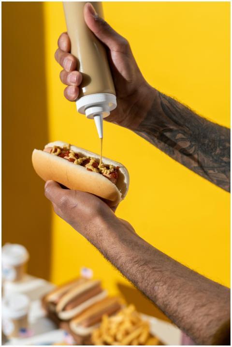 Person applying mustard to a hot dog with fries in
