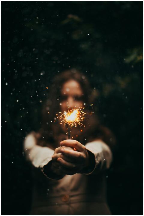 A young woman holds a sparkler outdoors at night,