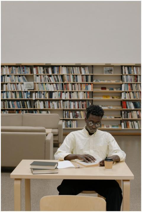 Young man studying at a library with bookshelves i