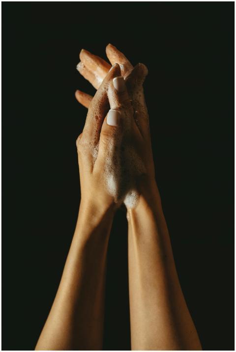 Close-up of hands lathered with soap against a bla