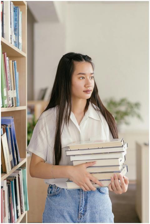 Teen student holding books in a library, dressed i