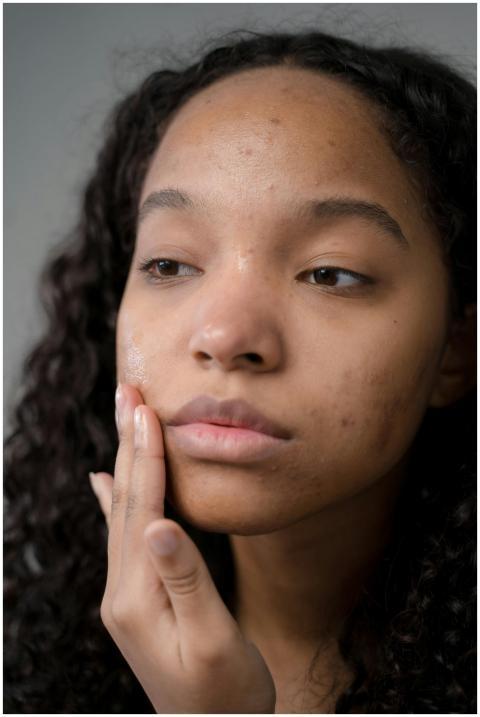 A thoughtful woman with curly hair examines her sk
