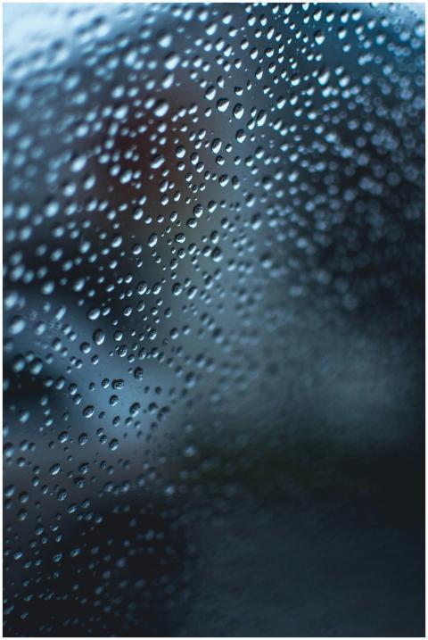 Close-up of raindrops on glass with a blue and tur